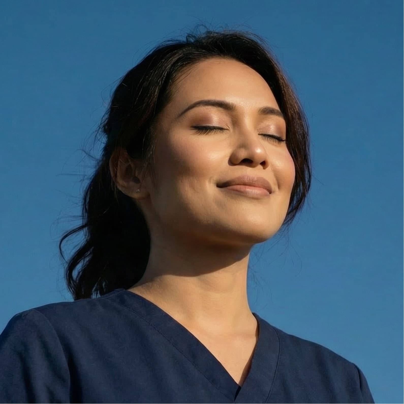 A doctor in scrubs, eyes closed, face lifted to the sun